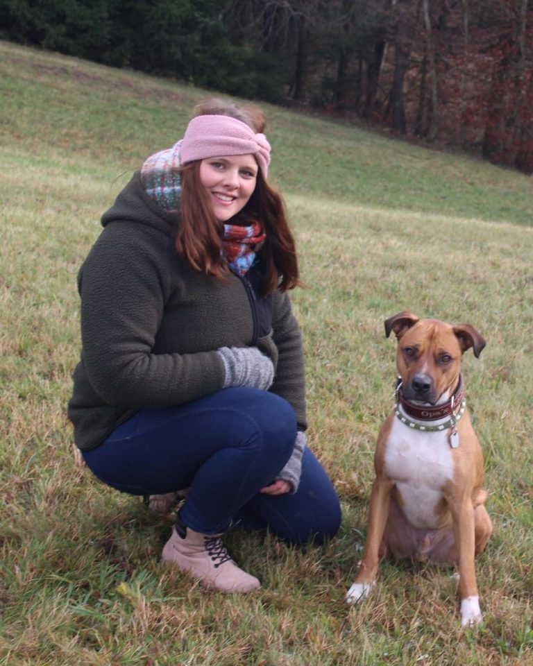 Frau kniet auf Wiese neben ihrem Hund, beide schauen freundlich in die Kamera. Frau kniet auf Wiese neben ihrem Hund, beide schauen freundlich in die Kamera.